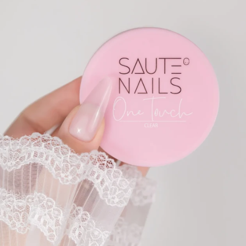 Tarro de gel de construcción Saute Nails One Touch Clear en mano con manicura profesional en tono rosa suave