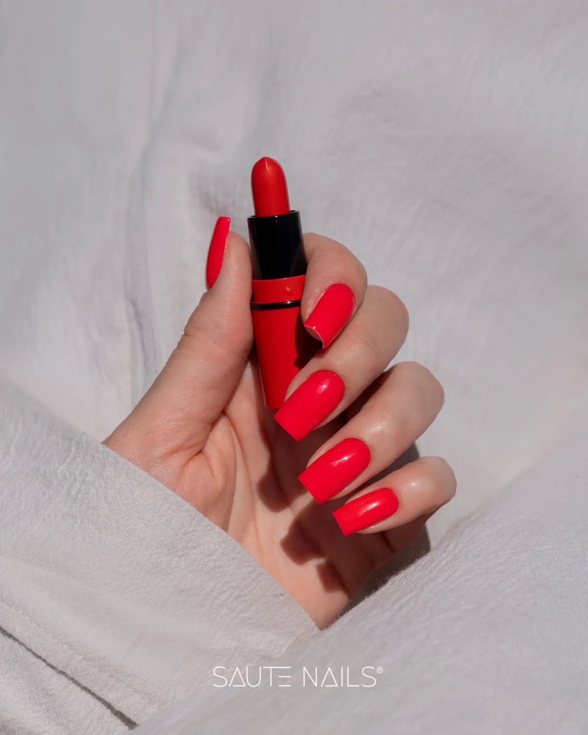 Mano con uñas largas cuadradas en rojo brillante sosteniendo una barra de labios roja